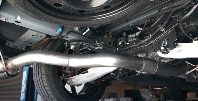 person installing new exhaust system under car 